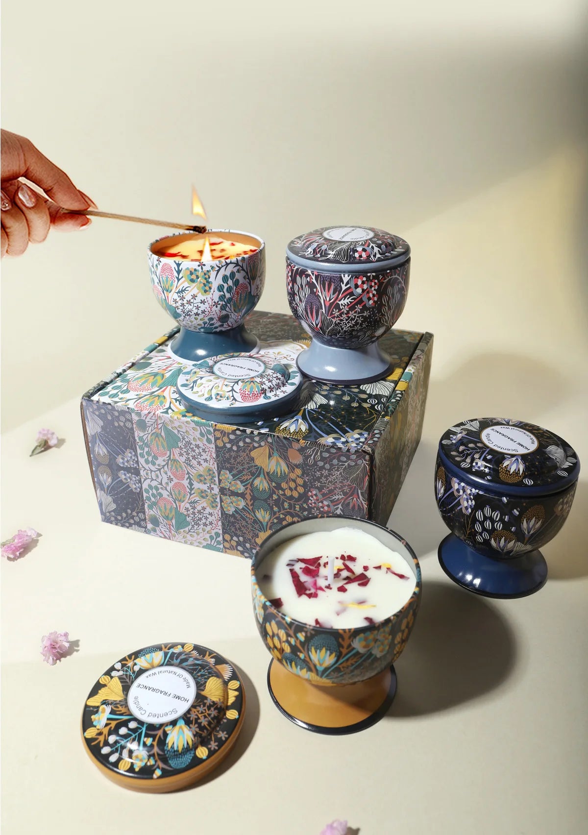 A set of soy wax aromatherapy candles in decorative tins and a lit candle being held by a hand.
