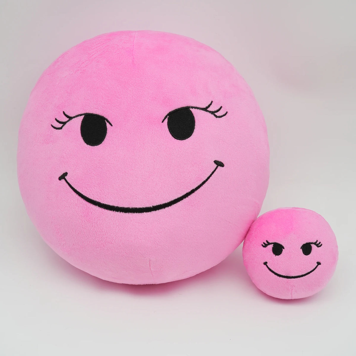A pink plush doll shaped like a smiling face with black eyes and mouth, used as a stress relief pillow.
