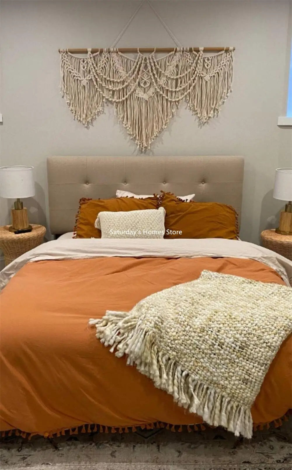 A handwoven boho macrame wall hanging tapestry in cream and beige hangs above a tan upholstered bed.