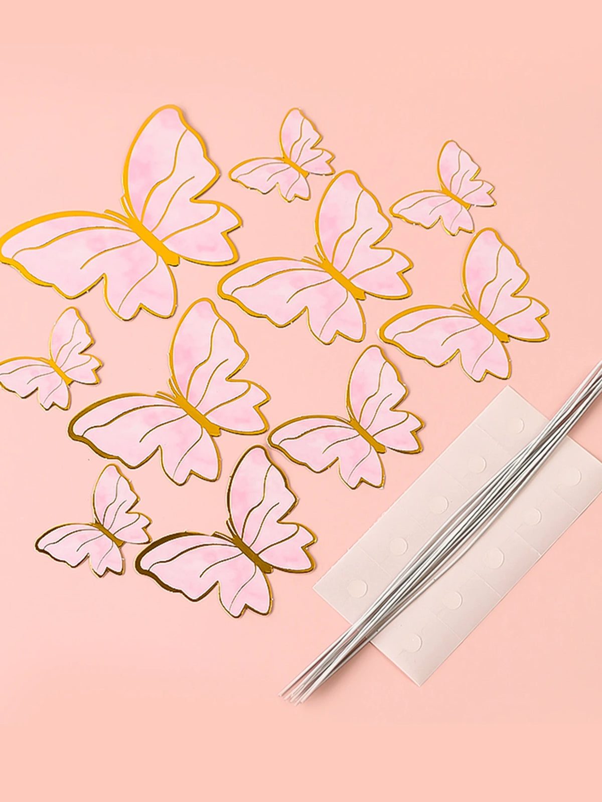 A set of pink and gold butterfly cake toppers scattered on a light pink background.