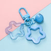 A collection of light blue and purple plastic charms and a keychain with a clasp on a pink and blue background.