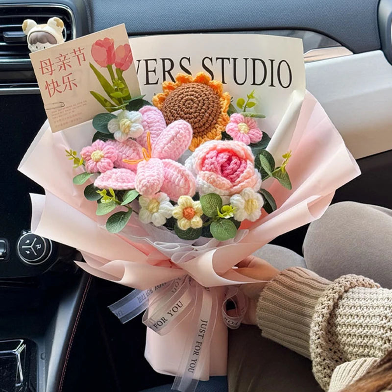A bouquet of pink and white handmade crochet flowers wrapped in sheer pink paper sits on a car interior.