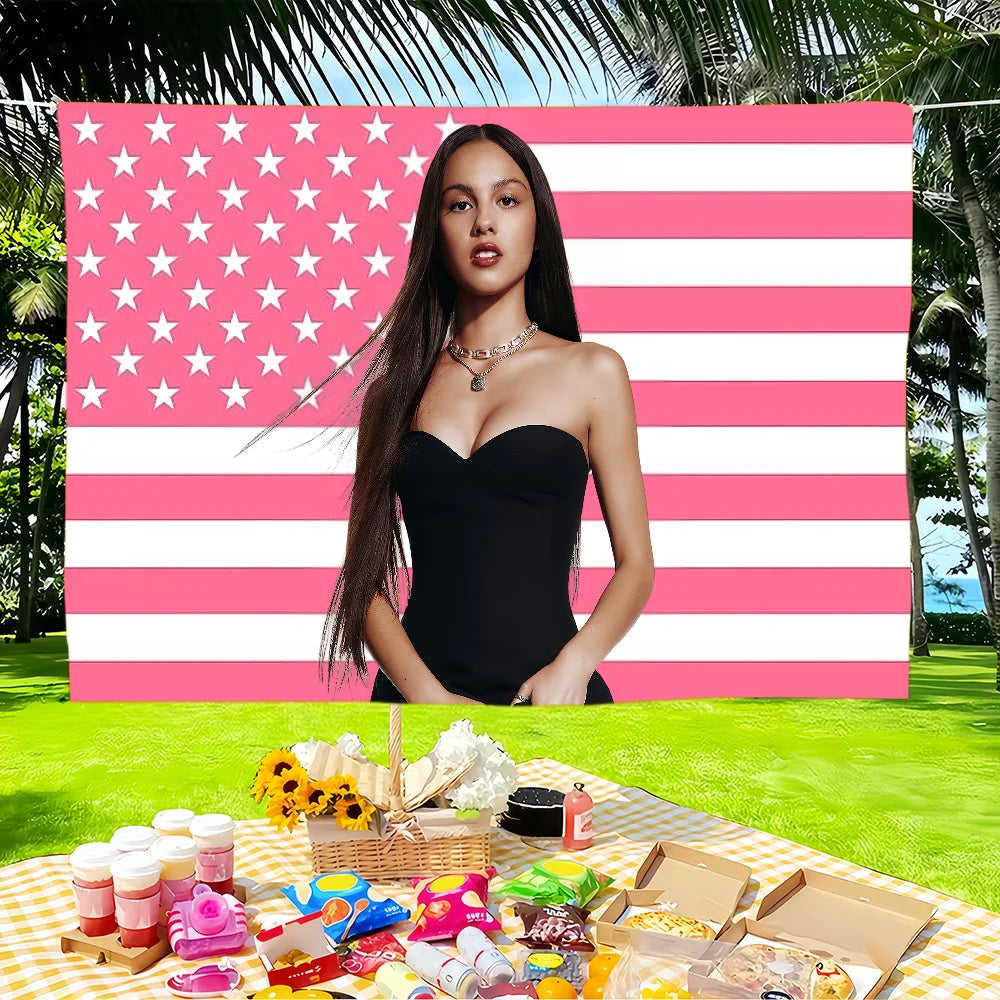 A woman posing in front of a large American flag tapestry with pink and white stripes and stars.