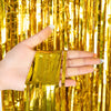 A hand holds several strands of metallic gold tinsel foil fringe curtain backdrop.