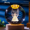 A clear glass crystal ball night light featuring a silhouette of an angel with wings glowing inside.
