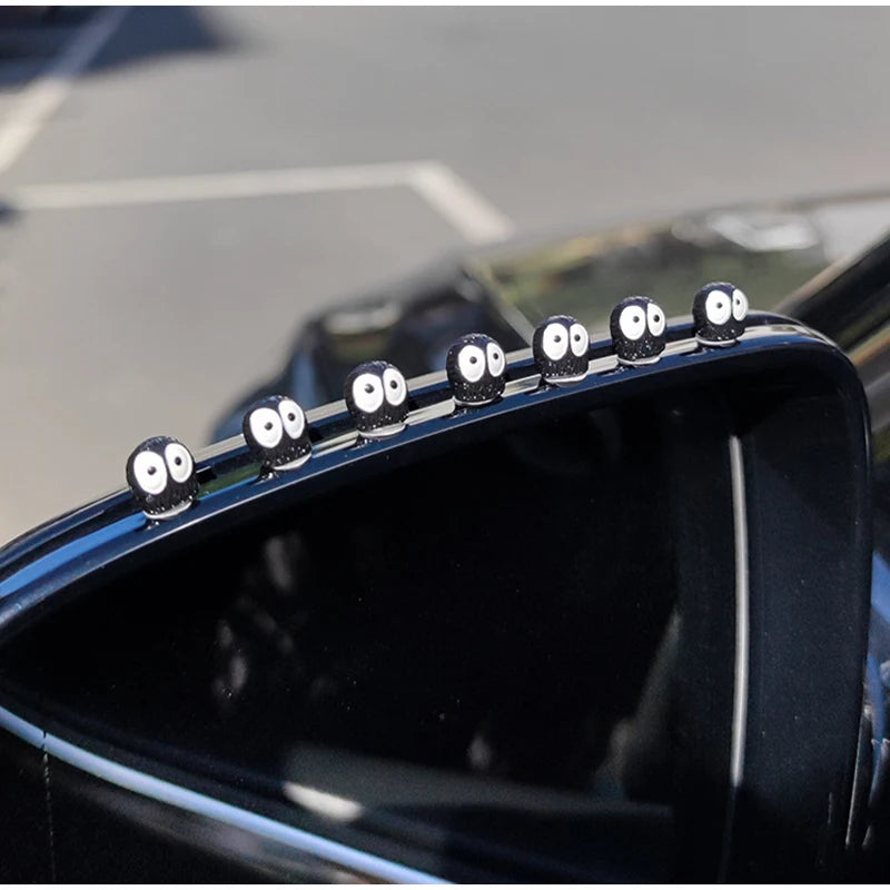 Gros plan sur le pare-chocs d'une voiture noire décoré de petits ornements en forme d'elfes ronds.