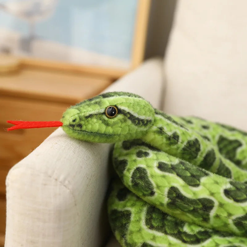 A bright green snake plush toy with a red forked tongue is resting on a white fabric surface.