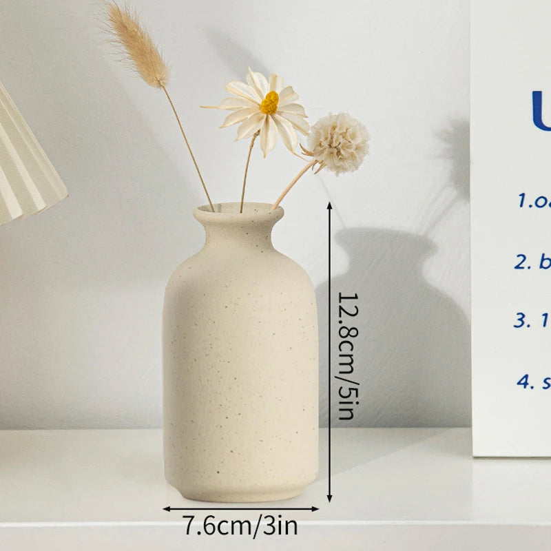 A minimalist ceramic vase in a light beige tone with dried floral arrangements on a white shelf.