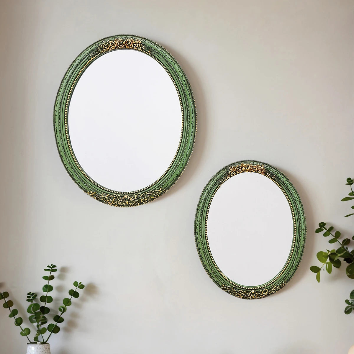 A round, oval wall mirror with a green frame and gold accents hanging on a light gray wall.