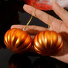 Two shiny orange pumpkin hanging ornaments are held in a hand against a dark background.