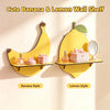A yellow banana-shaped wall shelf and a yellow lemon-shaped wall shelf displaying perfume bottles, a pink box, and a mirror.