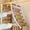 A hand is hanging folded beige pants on a multi-layer hanger with stainless steel rods against a light wall.