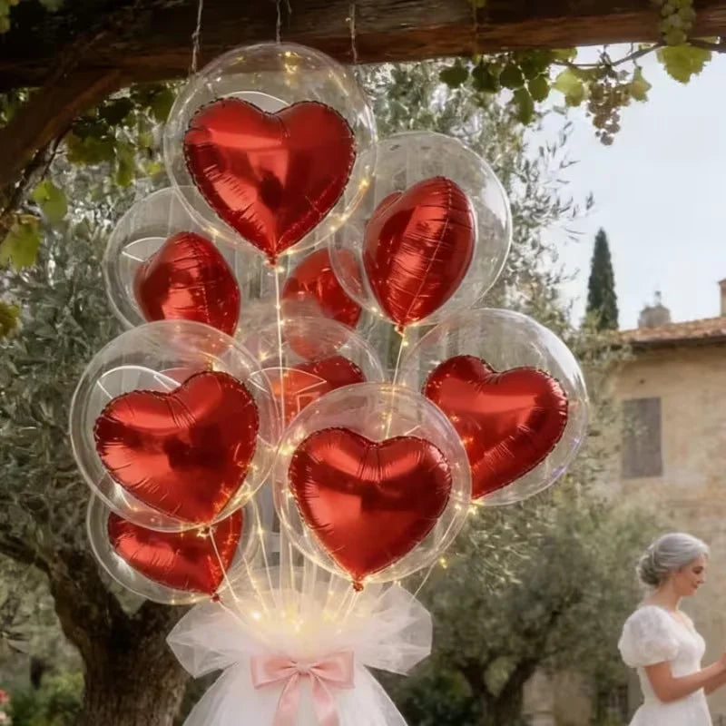 A set of red heart-shaped foil balloons and clear bubble balloons tied together, hanging from a tree branch.