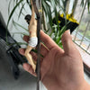 A hand holds a resin sculpture of an Easter cross crucifix wall hanging hanging from a branch amidst green foliage.