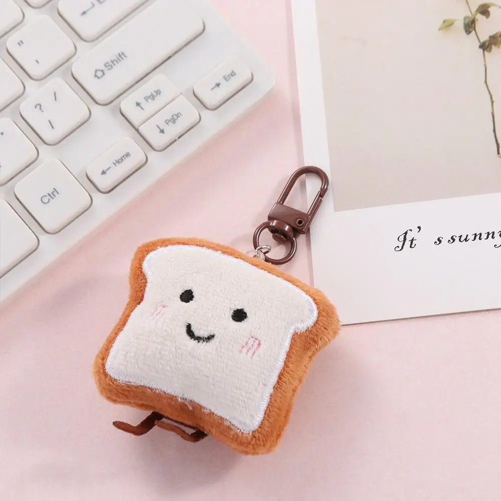 An adorable toast bread plush keychain charm resting on a pink surface next to a white laptop keyboard.