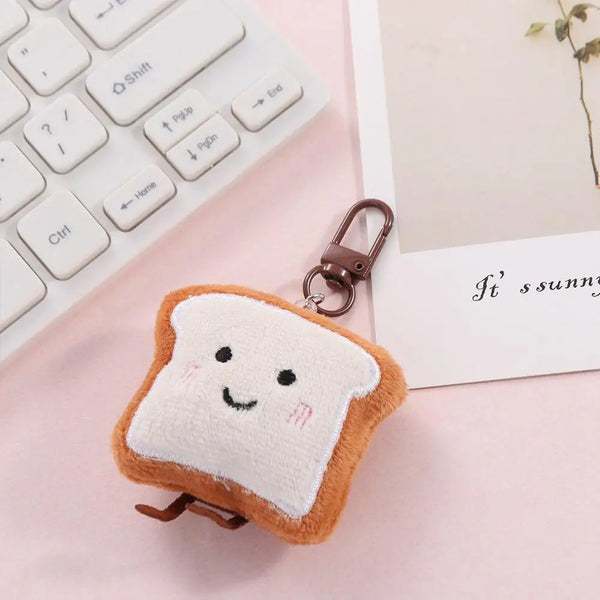 An adorable toast bread plush keychain charm resting on a pink surface next to a white laptop keyboard.