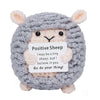 A handmade gray crochet sheep doll with pink ears holding an inspirational card.