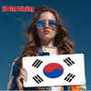 A woman holds a white metal plaque featuring the South Korean flag Taegeukgi design against a blue background.