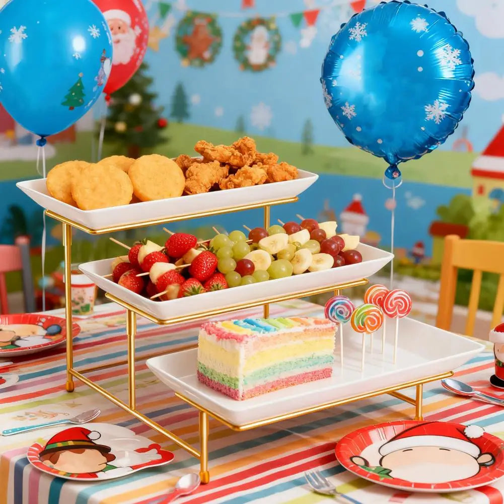 A gold-toned 3-tier serving rack displaying various foods like bread, fried chicken, and fruit on a colorful striped tableclo
