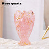 A pink rose quartz figurine shaped like a guardian angel with gold flecks on a white surface.