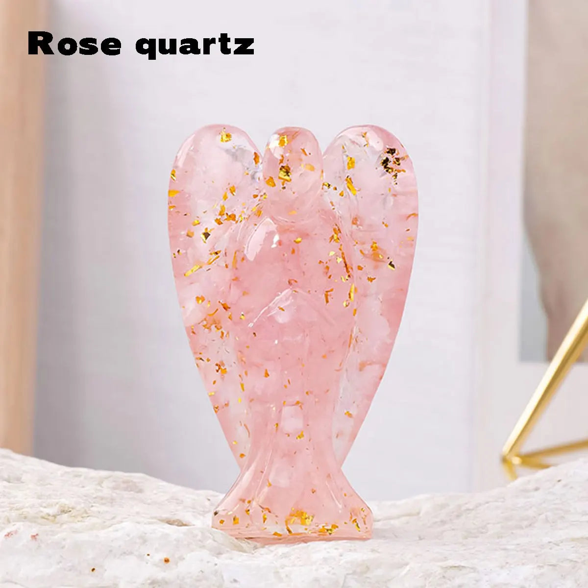 A pink rose quartz figurine shaped like a guardian angel with gold flecks on a white surface.