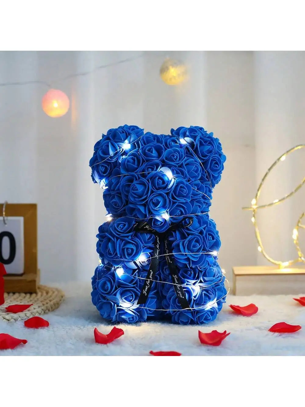 Blauer künstlicher Rosen-Teddybär, umhüllt von blauen Rosen, auf weißer Fläche mit sanftem Licht.