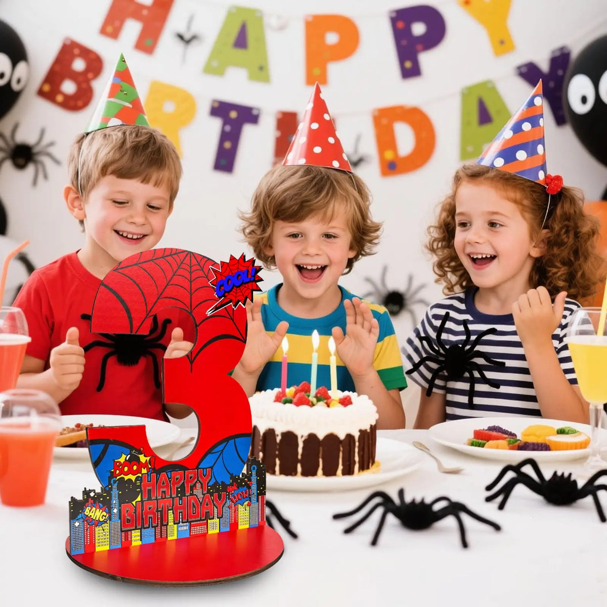 A birthday party setup featuring children, a cake, and a large wooden number sign shaped like a spider.