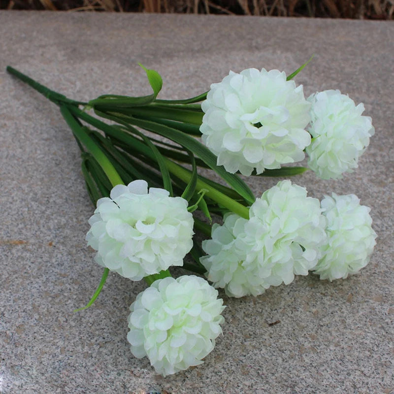 Un bouquet de fleurs d'hydrangea blanches artificielles posé sur une surface de pierre grise.