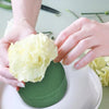 Hands place a creamy yellow floral foam block onto a round green foam block for flower arrangements.