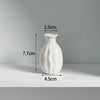 A white ceramic mini vase with a textured surface is shown on a shelf.