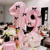 A large pink balloon set shaped like the number 19 with black bows displayed on a table setting.