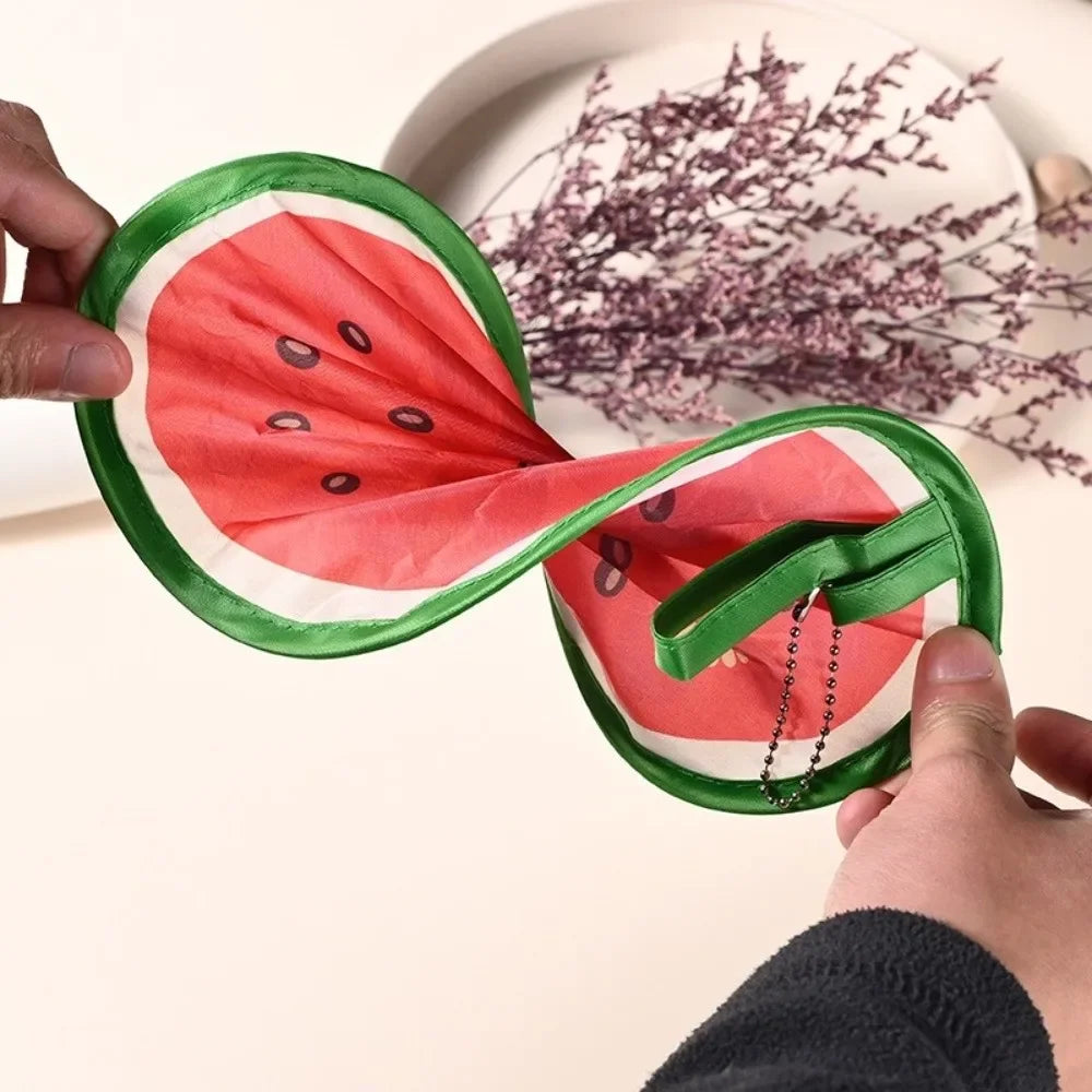 A hand is holding a foldable hand fan shaped like a sliced watermelon, green and red.