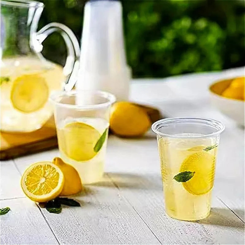 A glass of lemonade with a lemon slice is shown next to several disposable transparent plastic cups.