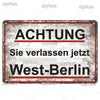 A vintage metal tin sign with a distressed gray background and red text that reads ACHTUNG Sie verlassen jetzt West-Berlin