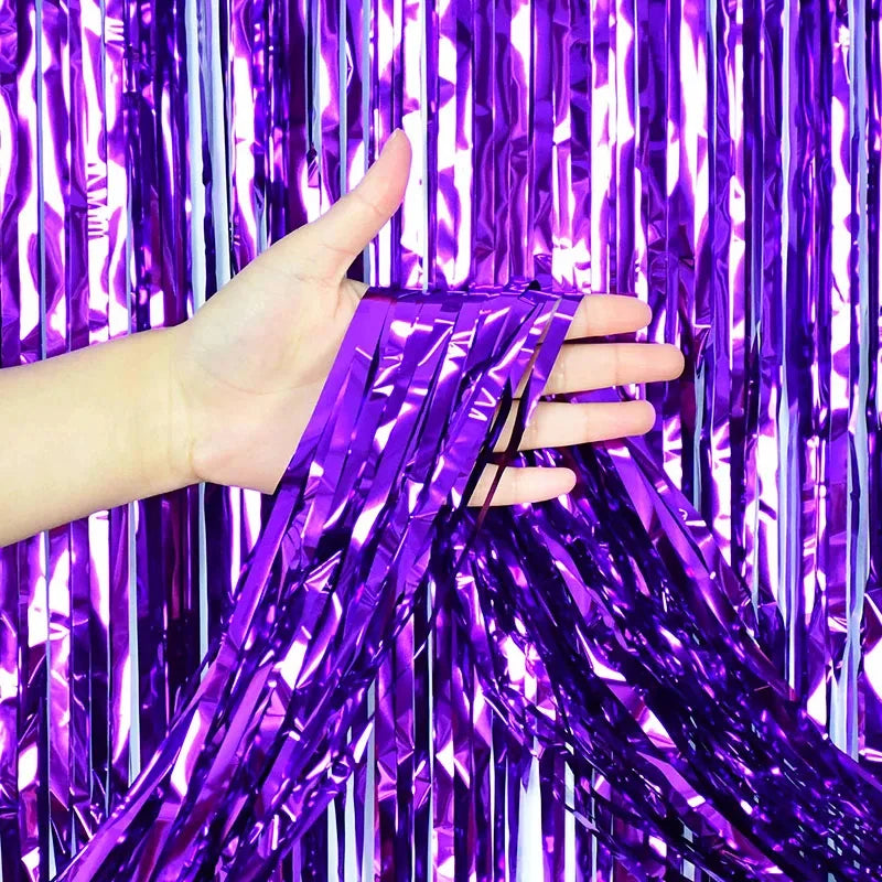 A hand is holding purple metallic foil fringe fabric against a vibrant purple curtain background.