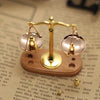 A vintage miniature balance scale with brass arms and glass pans rests on a wooden base.