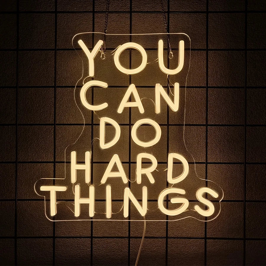 A glowing neon sign spelling out YOU CAN DO HARD THINGS against a dark grid background.