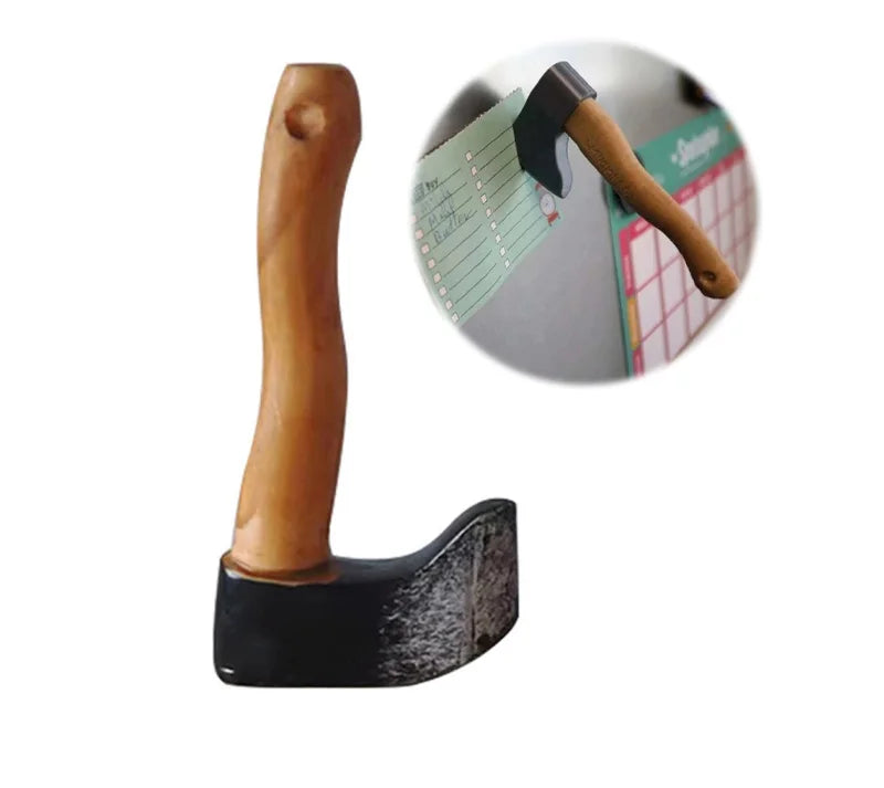 A wooden axe-shaped fridge magnet with a black handle and a green note attached.