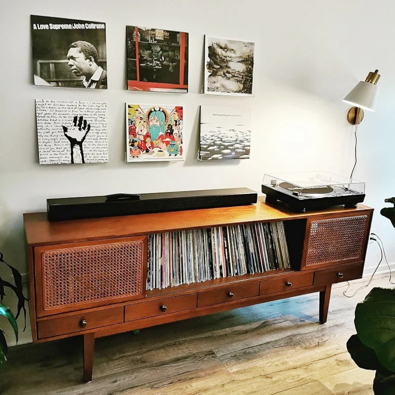 A wooden cabinet with a glass top and a section for vinyl records is displayed against a white wall with framed art.