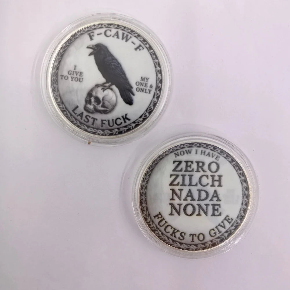 Two challenge coins featuring a crow and skull design with text related to 'last fuck' and 'zero zilch nada none'.