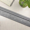 A silver self-adhesive 3D wall trim line with an ornate floral border placed on a light fabric surface.