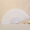 A white vintage lace folding fan with a delicate pattern is displayed on a light beige surface.