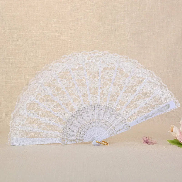 A white vintage lace folding fan with a delicate pattern is displayed on a light beige surface.