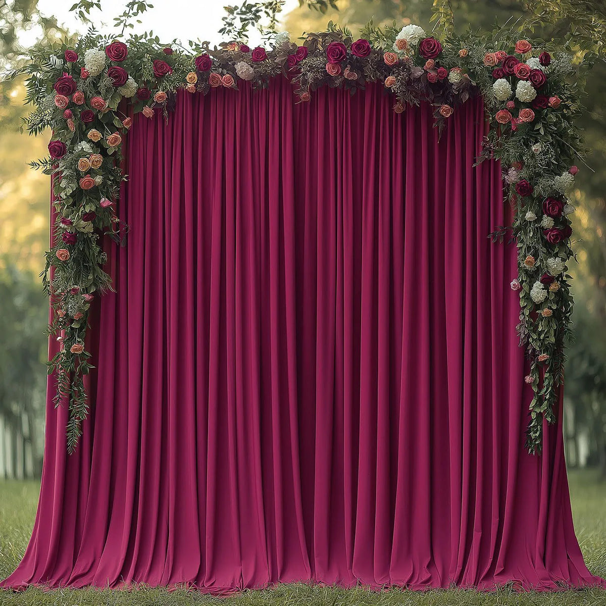 A deep magenta velvet drape backdrop decorated with lush greenery and dark pink floral arrangements for an event.