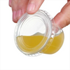 A hand is holding an open clear plastic sauce cup with a lid, showing a yellowish liquid inside.