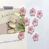 Pink and white decorative cherry blossom fridge magnets arranged on a light background.
