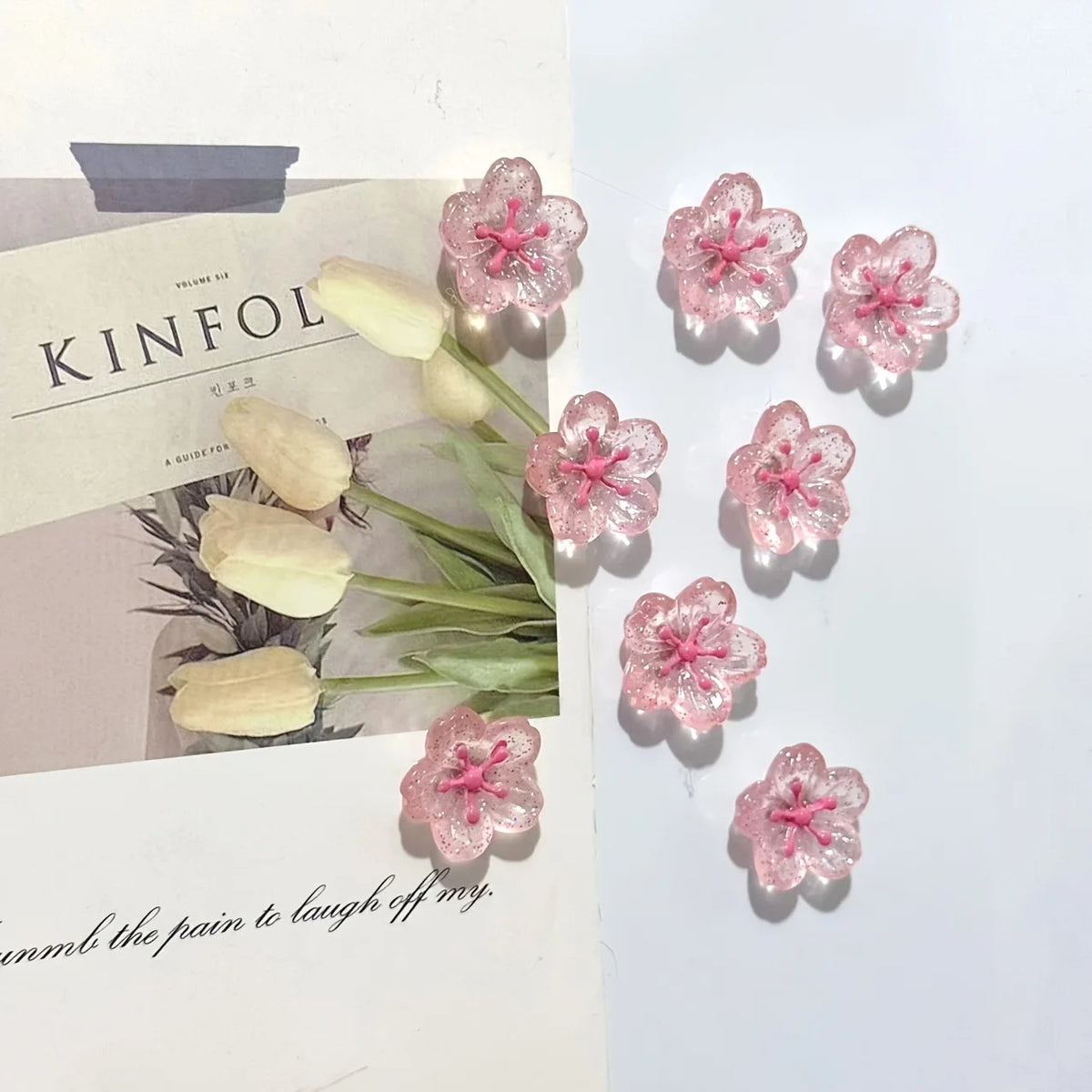 Pink and white decorative cherry blossom fridge magnets arranged on a light background.