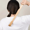 A person is using a bamboo back scratcher with a roller massager on their back.