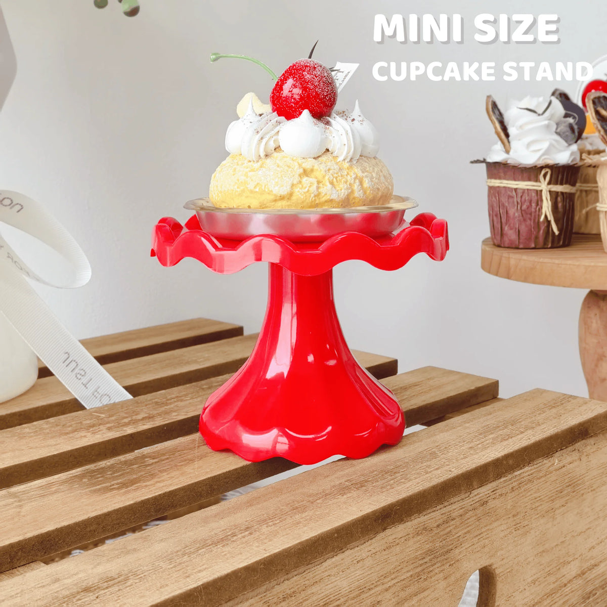 A red mini cupcake stand displaying a yellow cake with white frosting and a strawberry on a wooden surface.