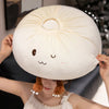 A woman is holding a large, round, cream-colored dumpling plush pillow with brown ears.